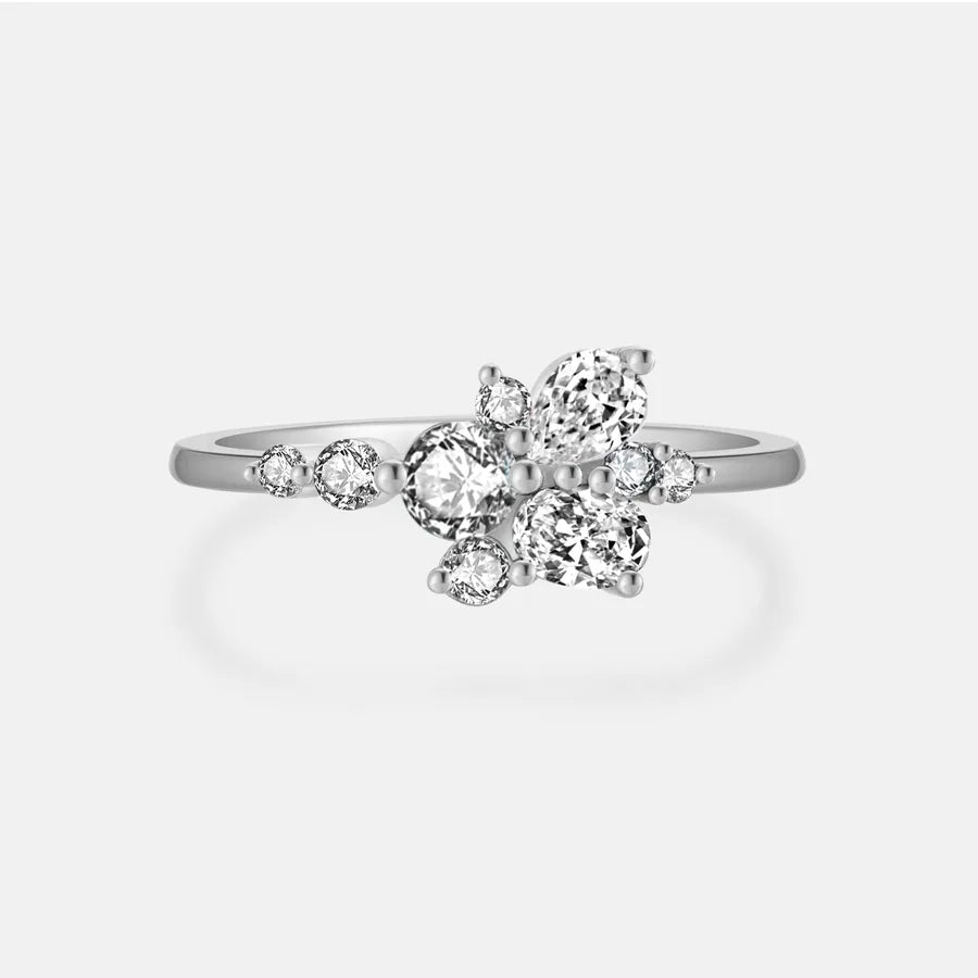 A silver-toned diamond ring with a floral cluster setting featuring marquise and round-cut clear stones, shown on a light gray background.