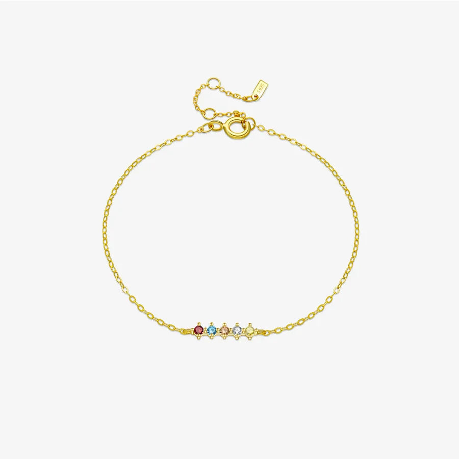 A delicate gold chain bracelet with a small central bar set with five colorful gemstones (red, green, blue, white, yellow) and an adjustable lobster clasp, shown on a light gray background.