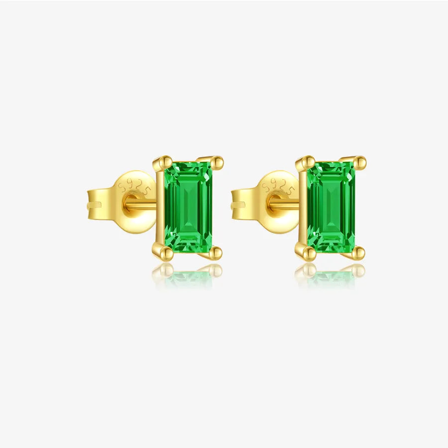 A pair of gold stud earrings with rectangular emerald-cut green gemstones, shown on a clean light gray background with a soft reflection below.