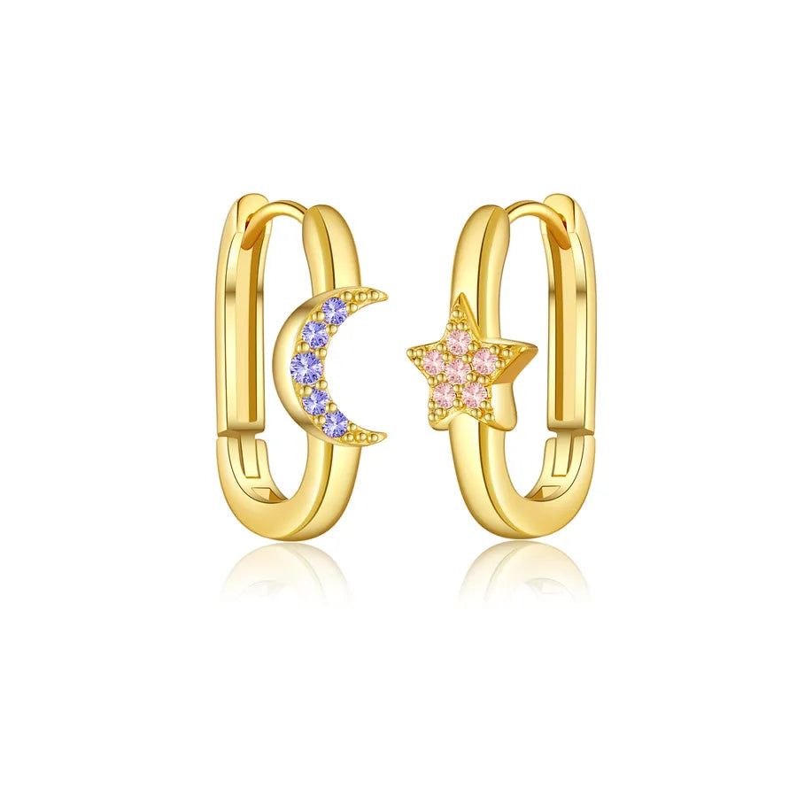 A pair of gold huggie hoop earrings, one decorated with a crescent moon paved with light blue stones and the other with a five-pointed star paved with light pink stones, set against a clean white background with a soft reflection.