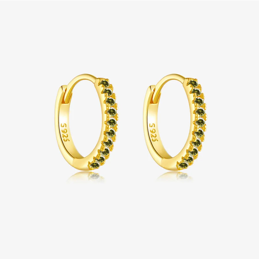 A pair of gold huggie hoop earrings with a row of small dark green gemstones set along the front, displayed on a clean white background with a subtle reflection.