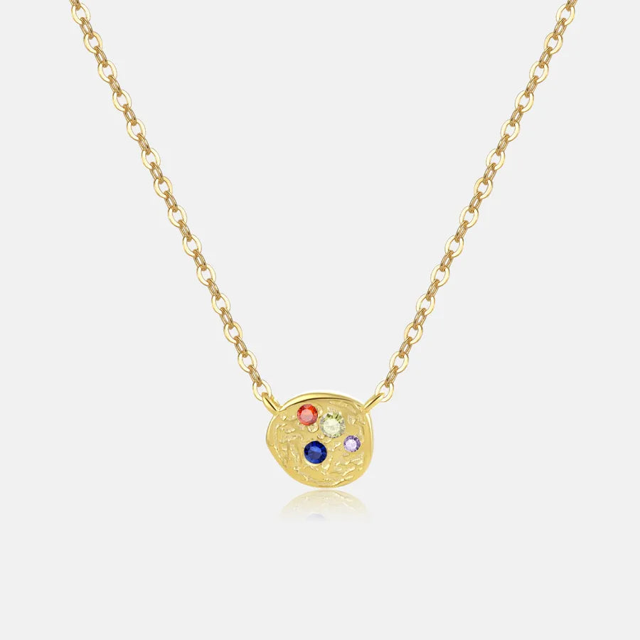 A gold chain necklace with a small, irregularly shaped gold pendant featuring five tiny colorful gemstones, displayed on a light gray background.