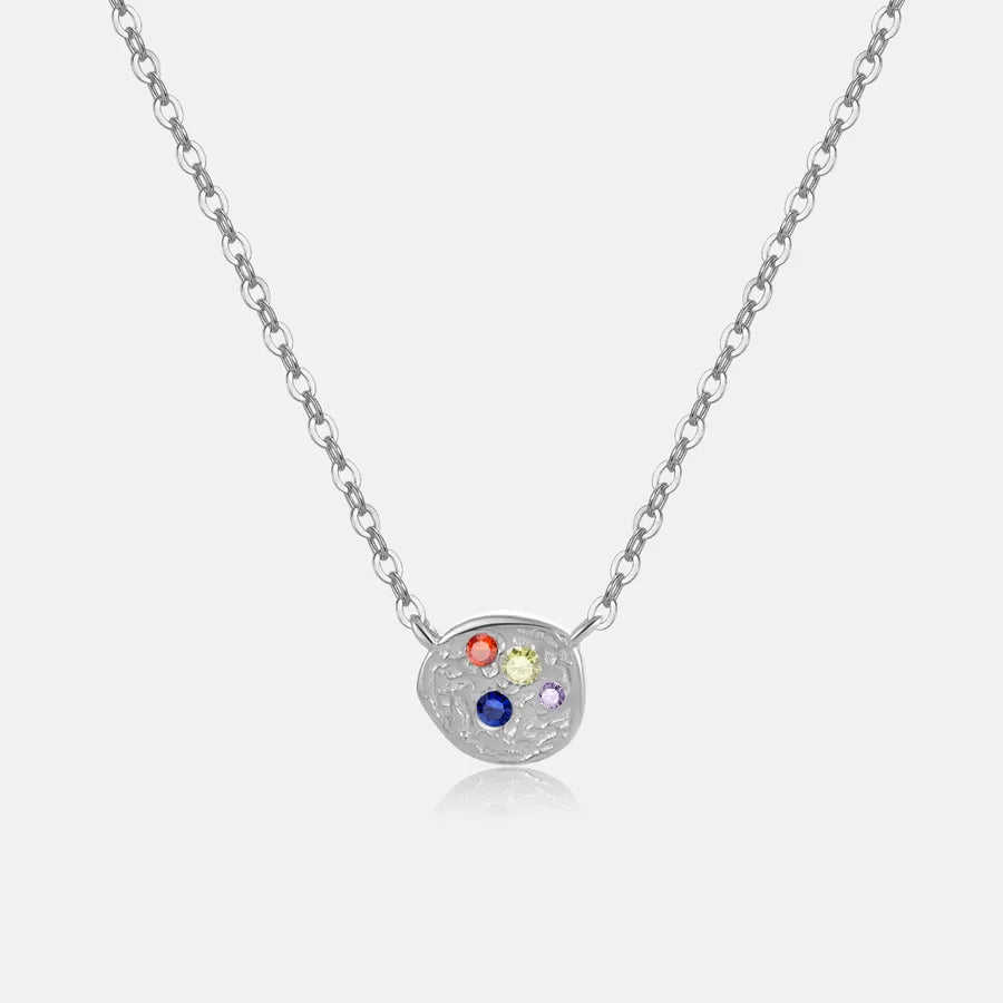 A silver chain necklace with an irregular, organic-shaped silver pendant featuring four small, colorful gemstones (red, yellow, blue, and purple) set against a light gray background.