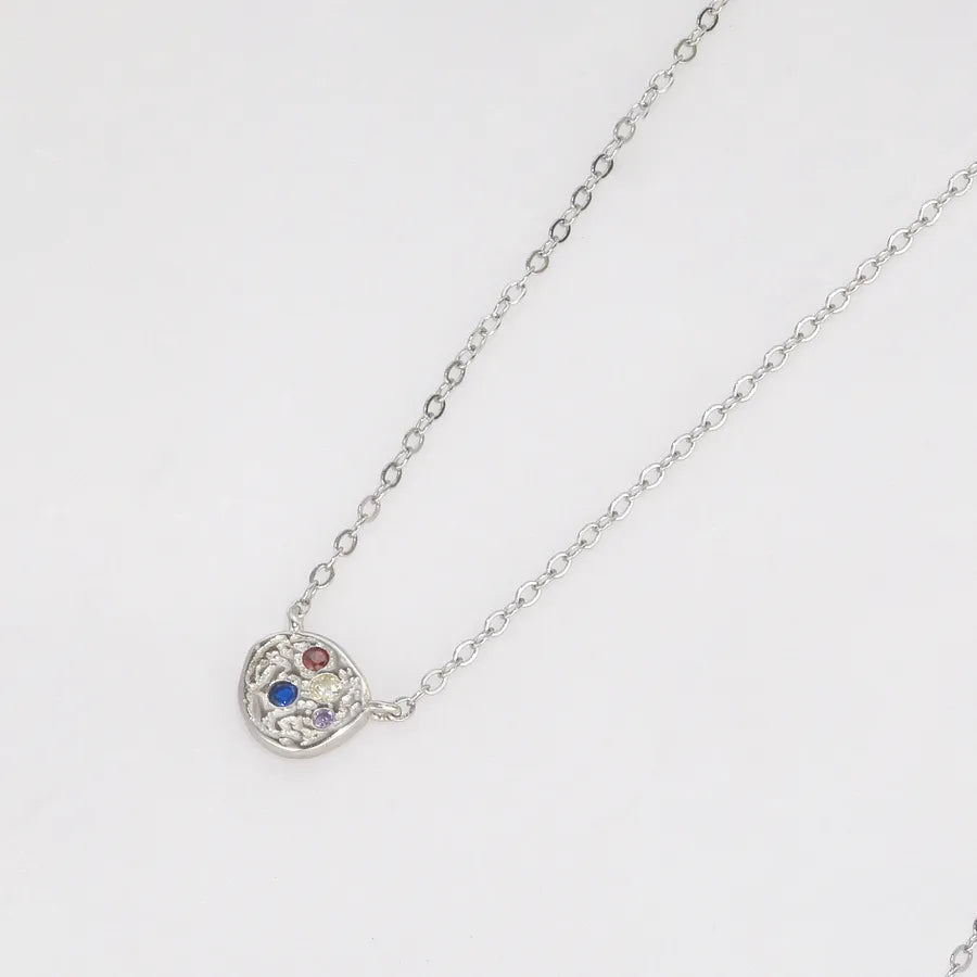 A silver chain necklace with a small, irregularly shaped silver pendant featuring three tiny colored gemstones (red, blue, and white), shown on a plain white background.