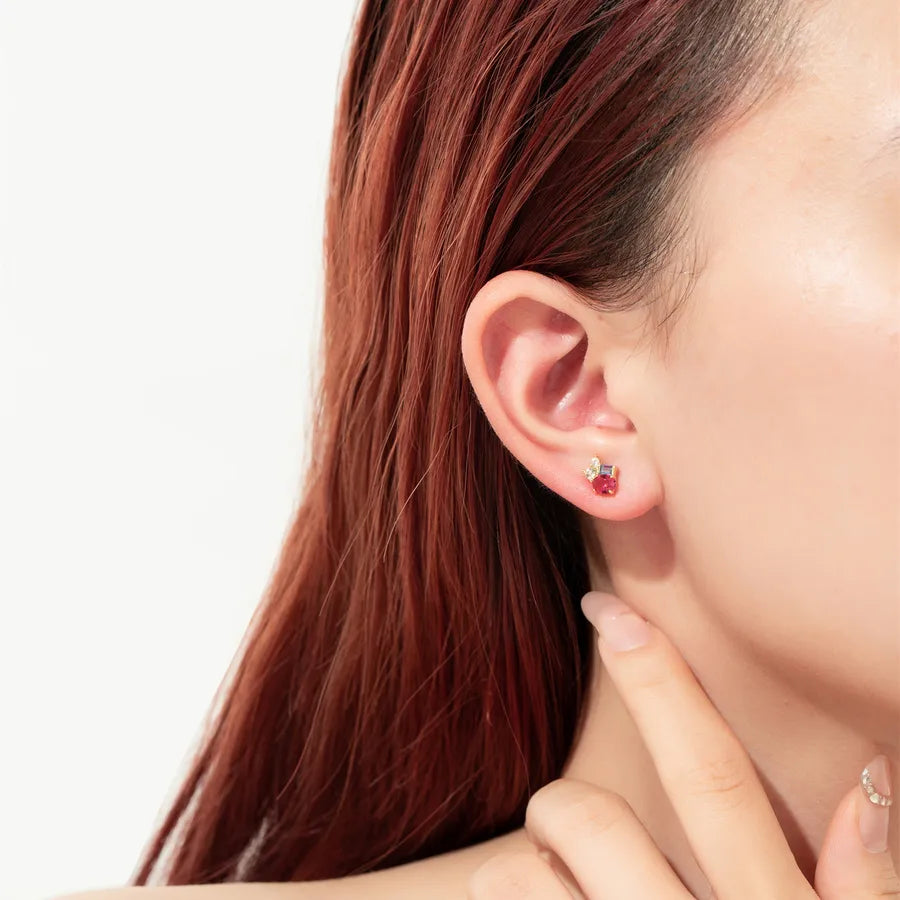 A close-up of a person's ear wearing a small stud earring with a red heart and a silver crescent moon, against a clean white background.