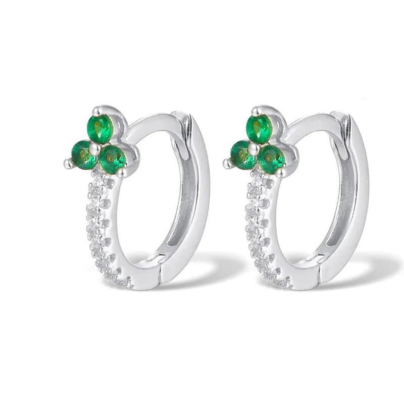 A pair of silver huggie hoop earrings featuring a small flower cluster of three green stones and a curved row of clear cubic zirconia crystals, shown on a white background.