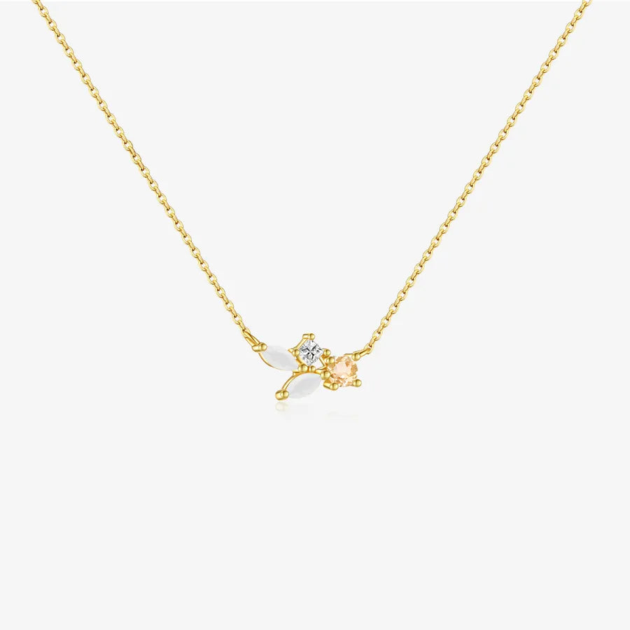 A delicate gold chain necklace featuring a small pendant with a clear round gemstone and a peach-colored heart-shaped gemstone, set against a clean white background.