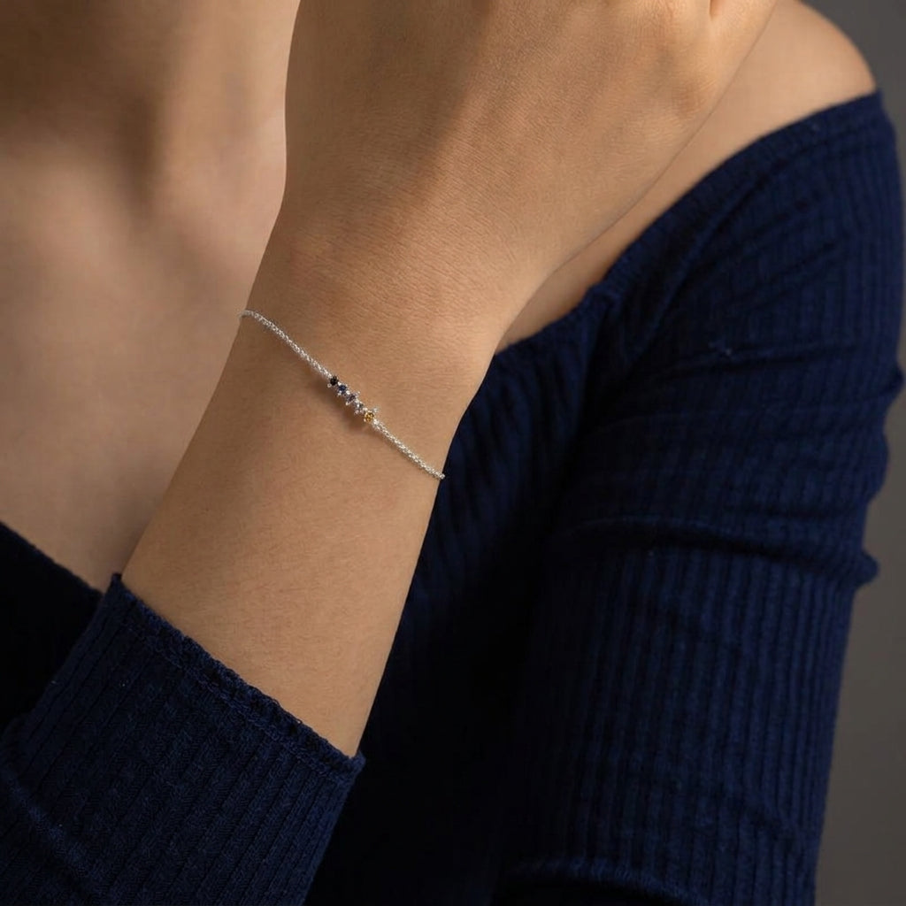 A delicate silver chain bracelet with a small central cluster of dark blue, white, and gold beads, shown worn on a person's wrist.