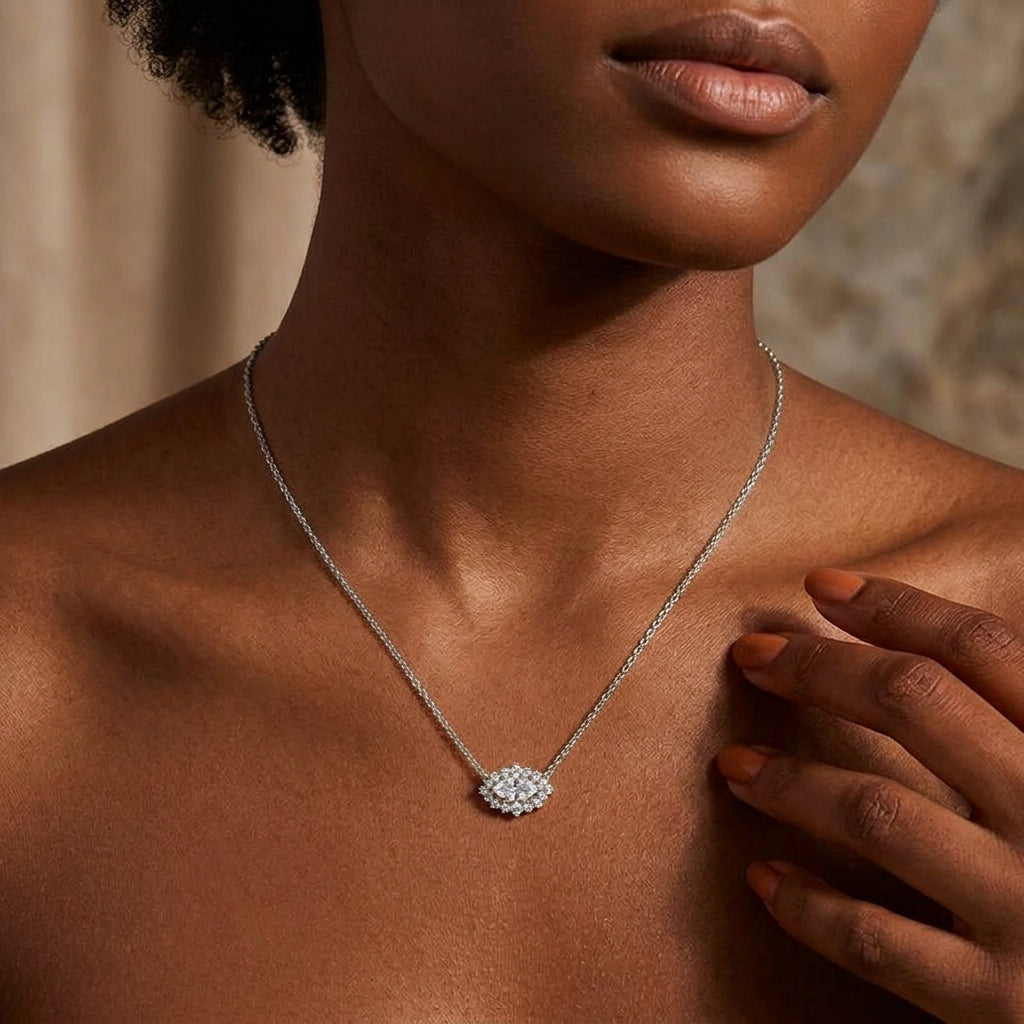 A close-up lifestyle shot of a model wearing a delicate silver chain necklace with a small, round, diamond-like cluster pendant on a warm, neutral background.
