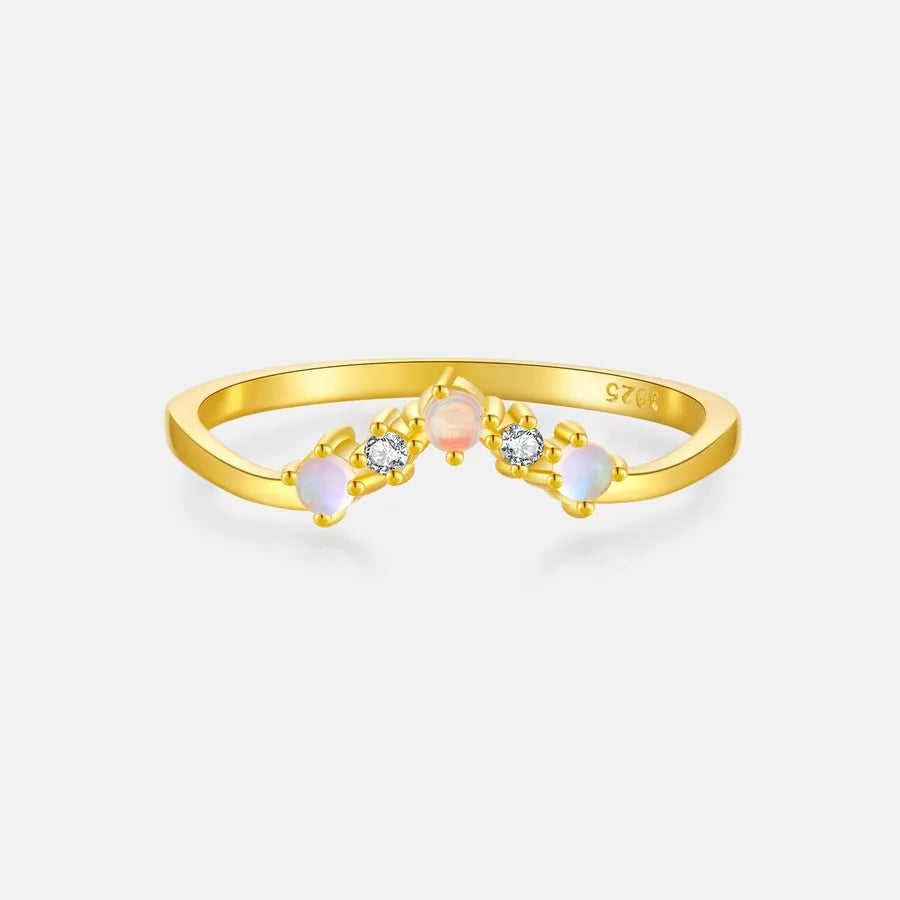 A gold ring with three small floral clusters, featuring clear round-cut stones and two iridescent opal-like beads in pale pink, white, and light blue, set against a light gray background.