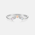 A silver ring featuring three small opal-like gemstones in prong settings, with one peach-colored stone and two iridescent white stones, on a light gray background.