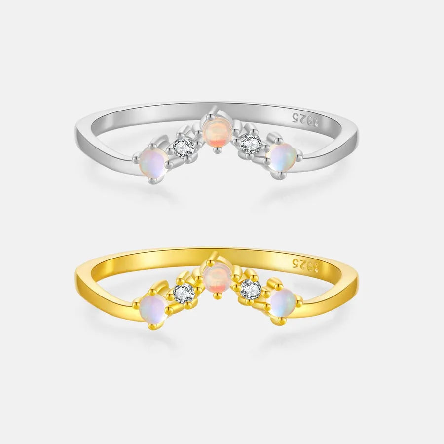 Two slim rings on a light gray background: a silver ring with three iridescent opal-like stones and two clear stones, and a yellow gold ring with the same opal-like stones and clear stones. Both rings show a 925 sterling silver/gold mark inside.