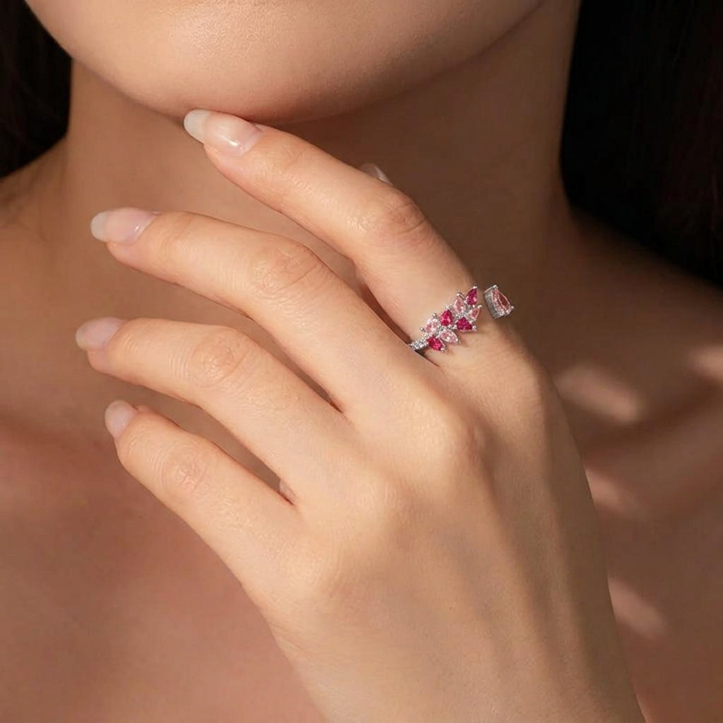 A close-up of a woman's hand wearing a delicate ring with small pink gemstones and clear stones on a silver-toned band.
