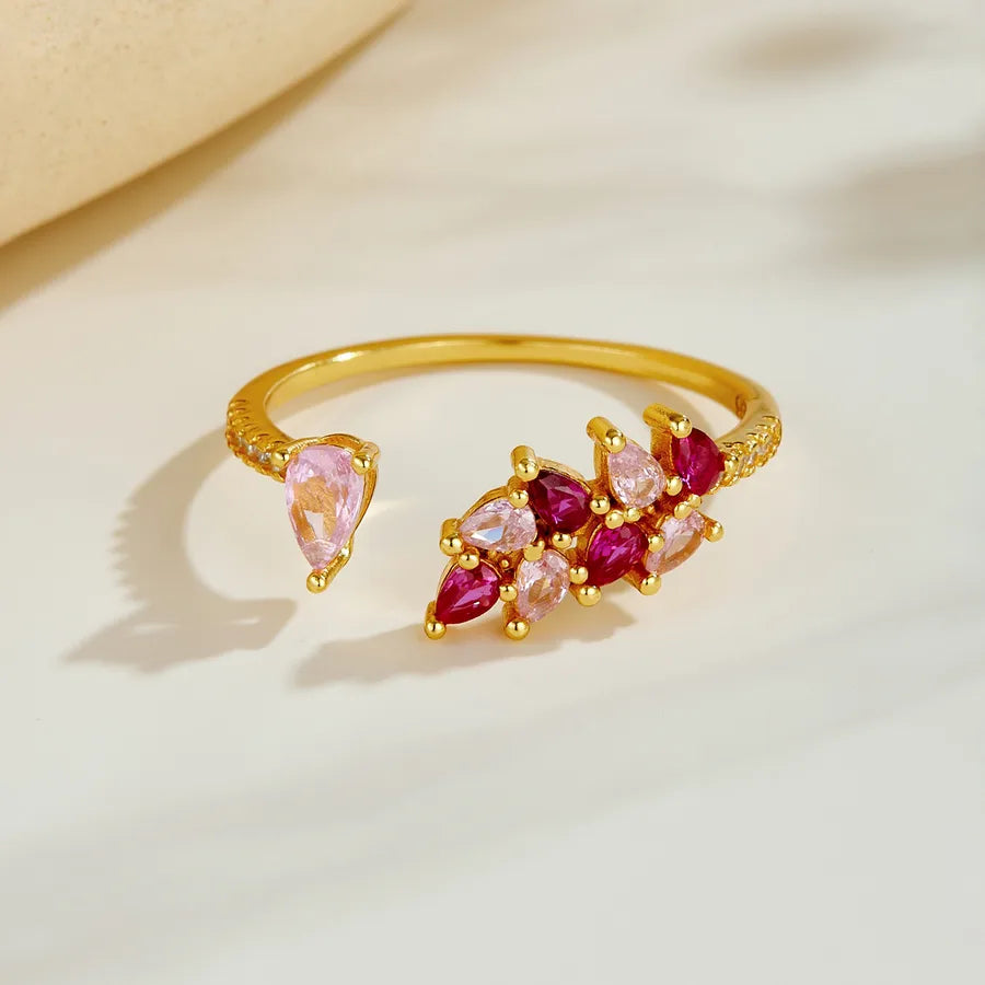 Gold open cuff ring with pink and magenta marquise-cut gemstones, displayed on a light beige surface.