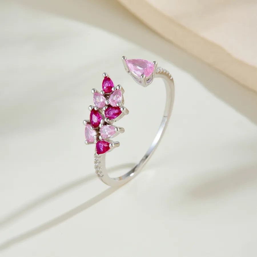A silver open ring ring featuring a cluster of pink marquise-cut gemstones and a single larger pink marquise gemstone on the upper right, photographed on a soft cream surface.