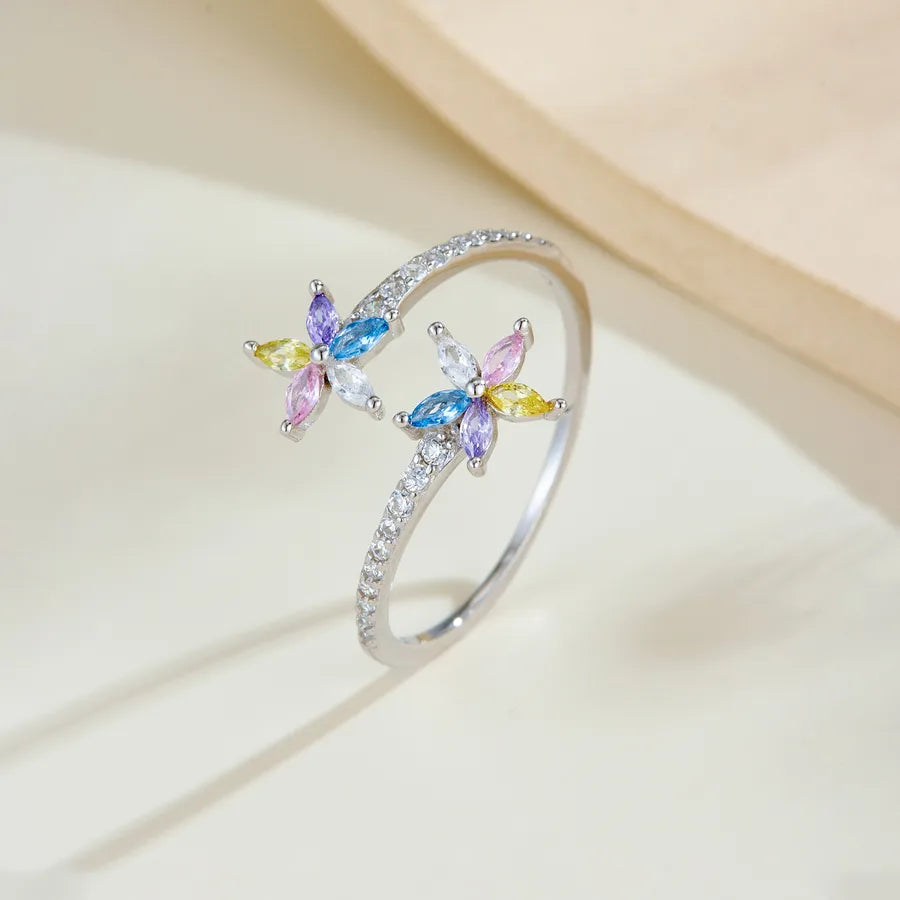 A silver open ring ring decorated with two butterfly charms, each featuring marquise-cut crystals in blue, purple, pink, and yellow, accented by small clear stones along the band.