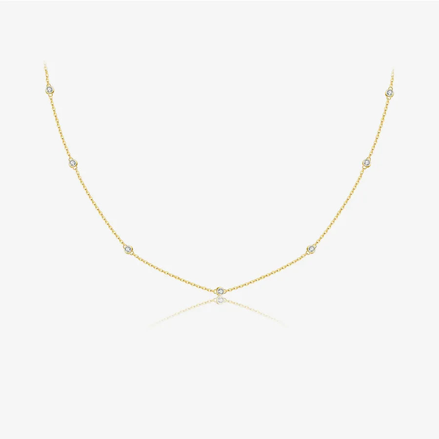 A delicate yellow gold chain necklace featuring small, evenly spaced round-cut clear gemstones, displayed on a clean white background with a subtle reflection.