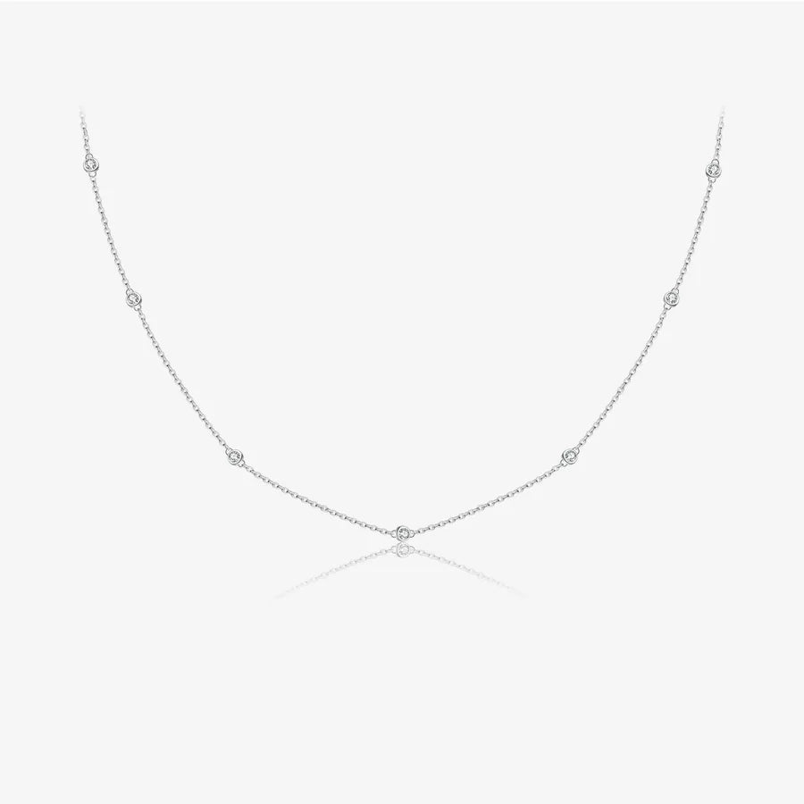 A delicate silver chain necklace with small, evenly spaced round bezel-set clear stones, displayed on a clean white background with a faint reflection below.