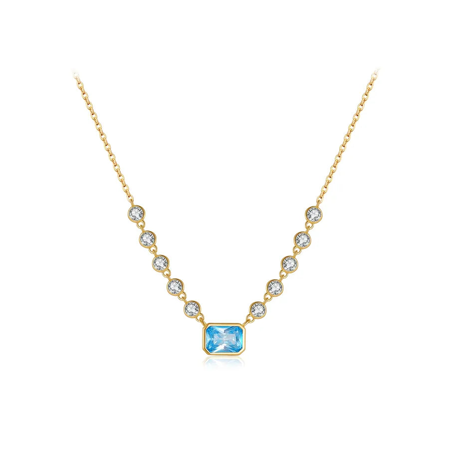 A gold necklace featuring a central rectangular light blue gemstone pendant, flanked by smaller round clear stones in bezel settings along the chain, shown on a plain white background.