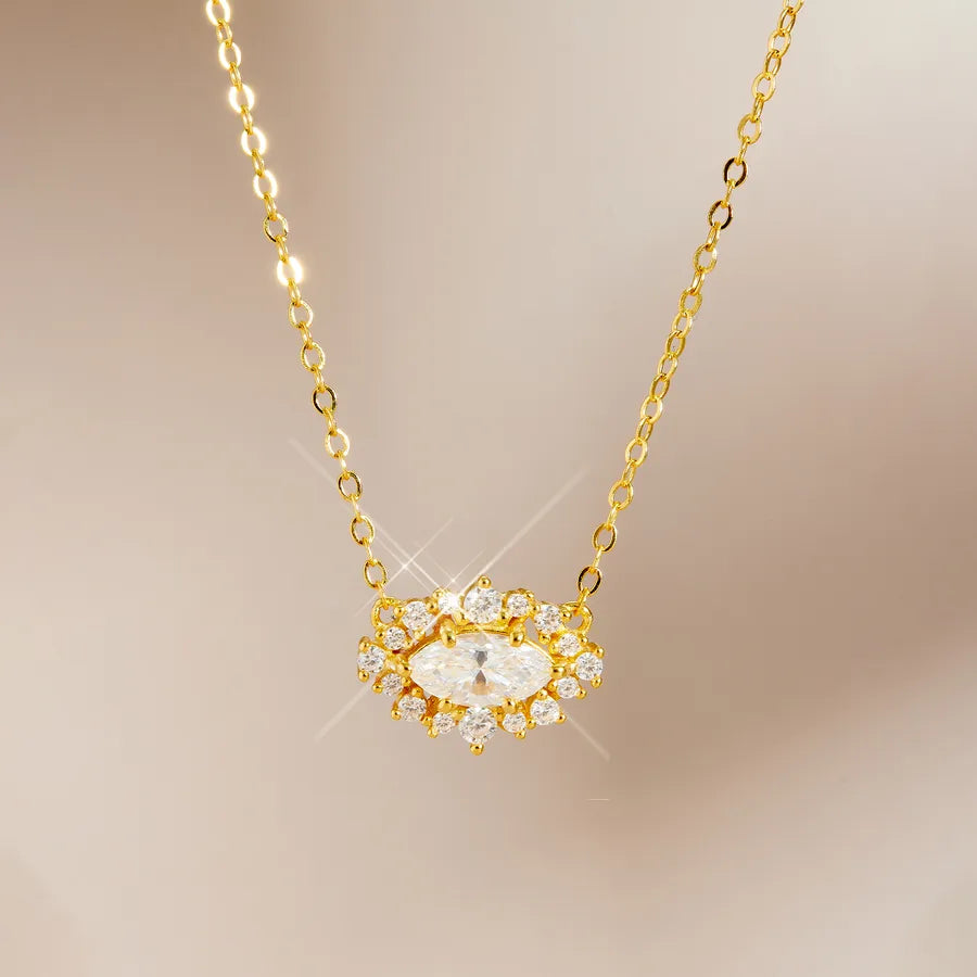Gold chain necklace with a heart-shaped pendant featuring a large clear marquise-cut center stone surrounded by small clear round stones in a gold setting, shown on a soft beige background.
