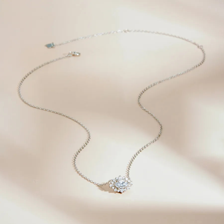 A delicate silver chain necklace with a small, clear crystal flower-shaped pendant, displayed on a soft beige background with elegant shadows.