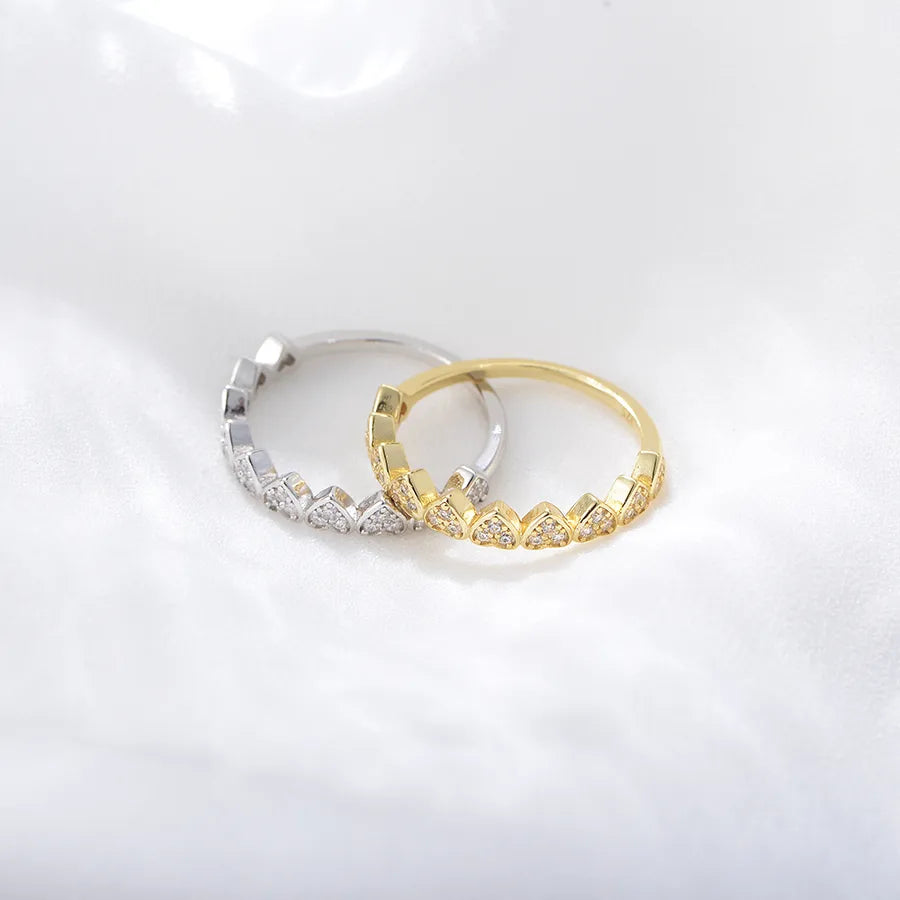 Two hoop rings with a chevron heart pattern of small clear stones, one in yellow gold and one in silver, displayed on a soft white fabric background.