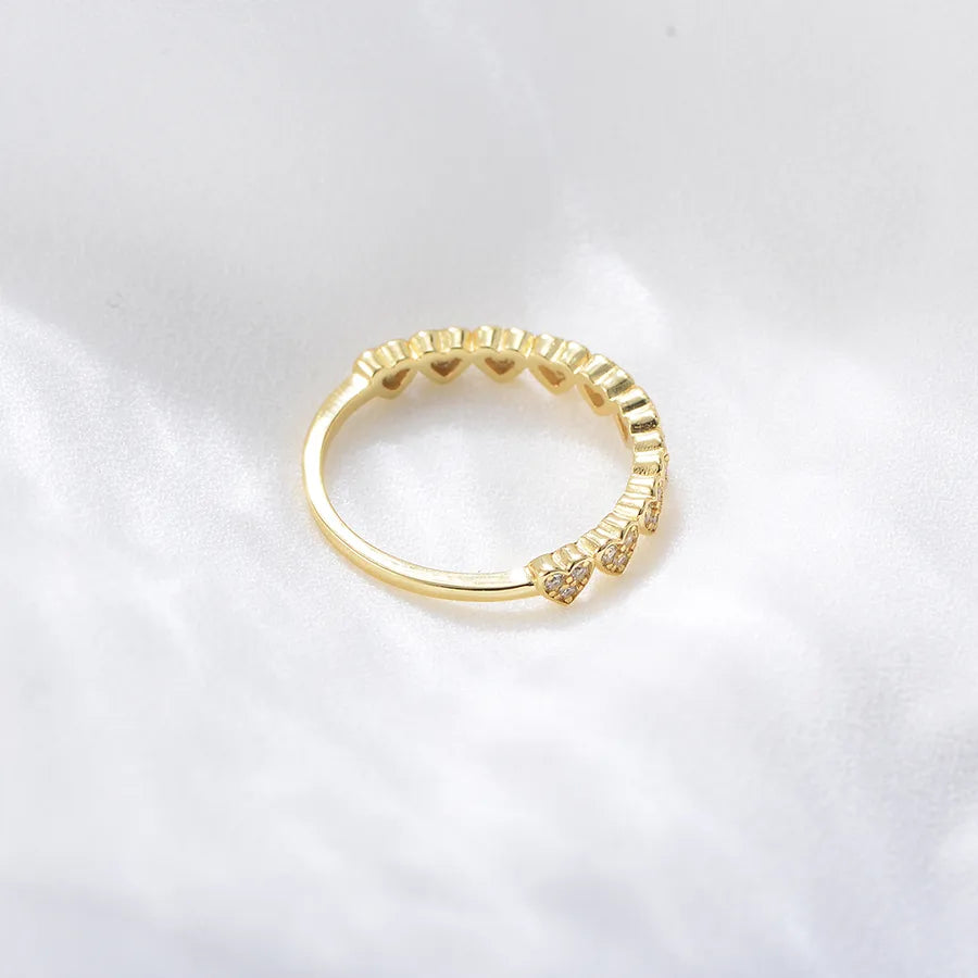 A gold ring with a textured, scalloped outer edge and small clear stones, photographed on a soft white fabric background.