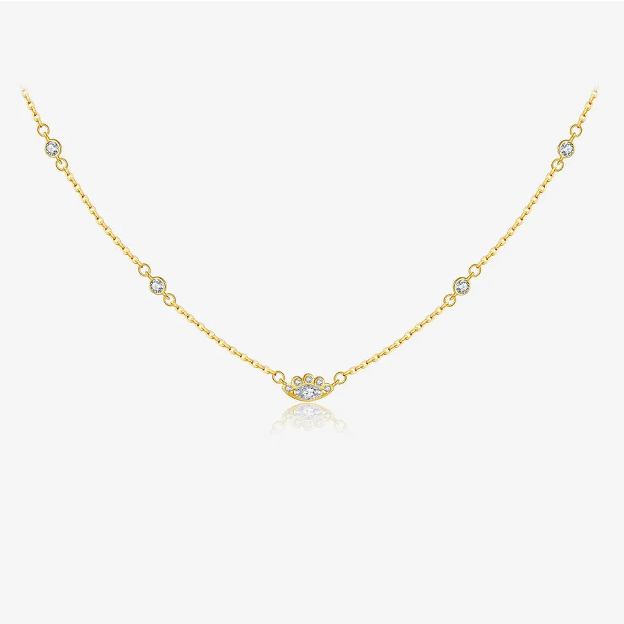 A delicate gold chain necklace featuring a central cluster of clear round-cut stones and small bezel-set clear stones spaced along the chain, displayed on a light gray background with a soft reflection.