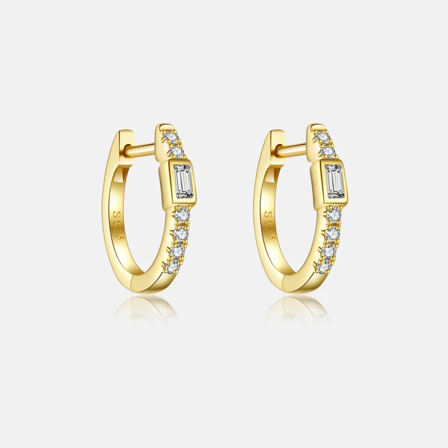 A pair of gold huggie hoop earrings with a central rectangular bezel-set clear stone and rows of small clear stones along the outer band, shown on a light gray background.