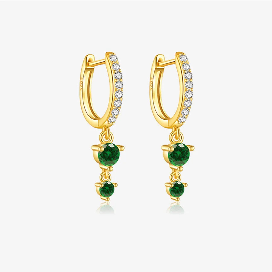 A pair of gold huggie hoop earrings with a row of clear pavé stones along the front curve and three dangling green gemstones on each earring, shown on a light gray background.