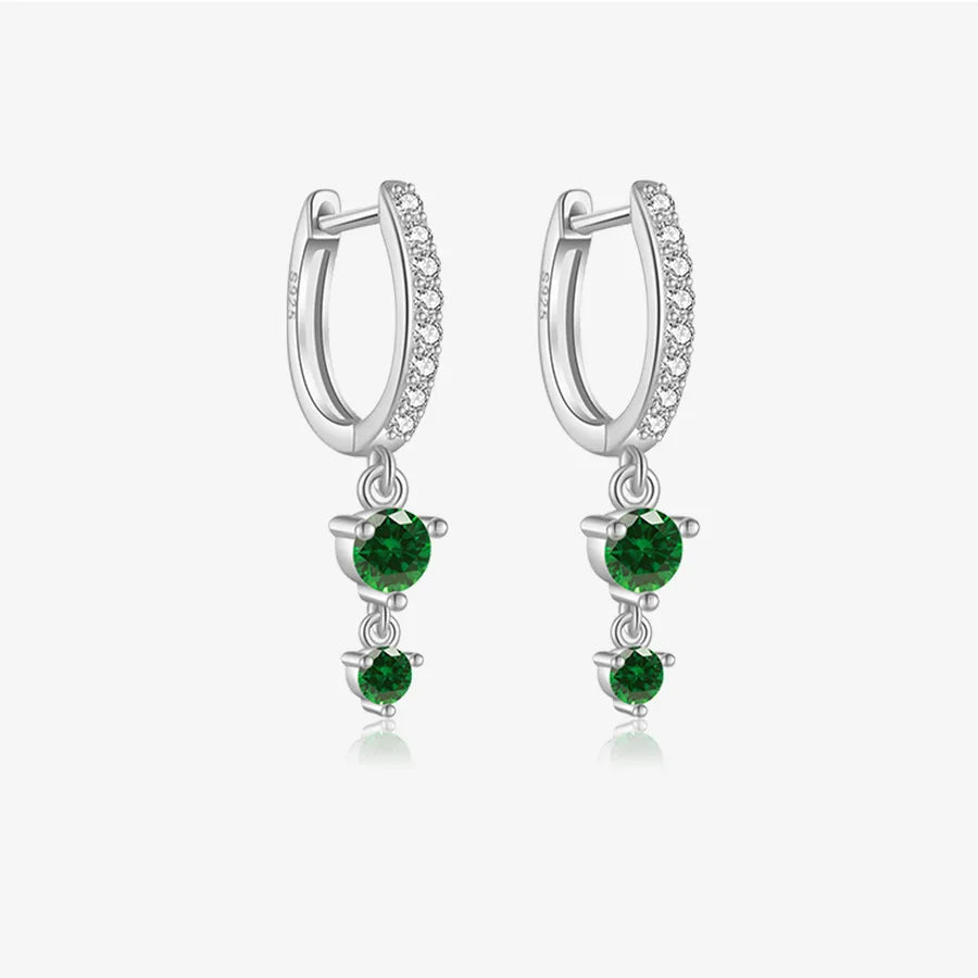 A pair of silver huggie hoop earrings with a row of small clear stones along the front, and each hoop hangs a dangling cluster of three round green gemstones, shown on a light gray background.