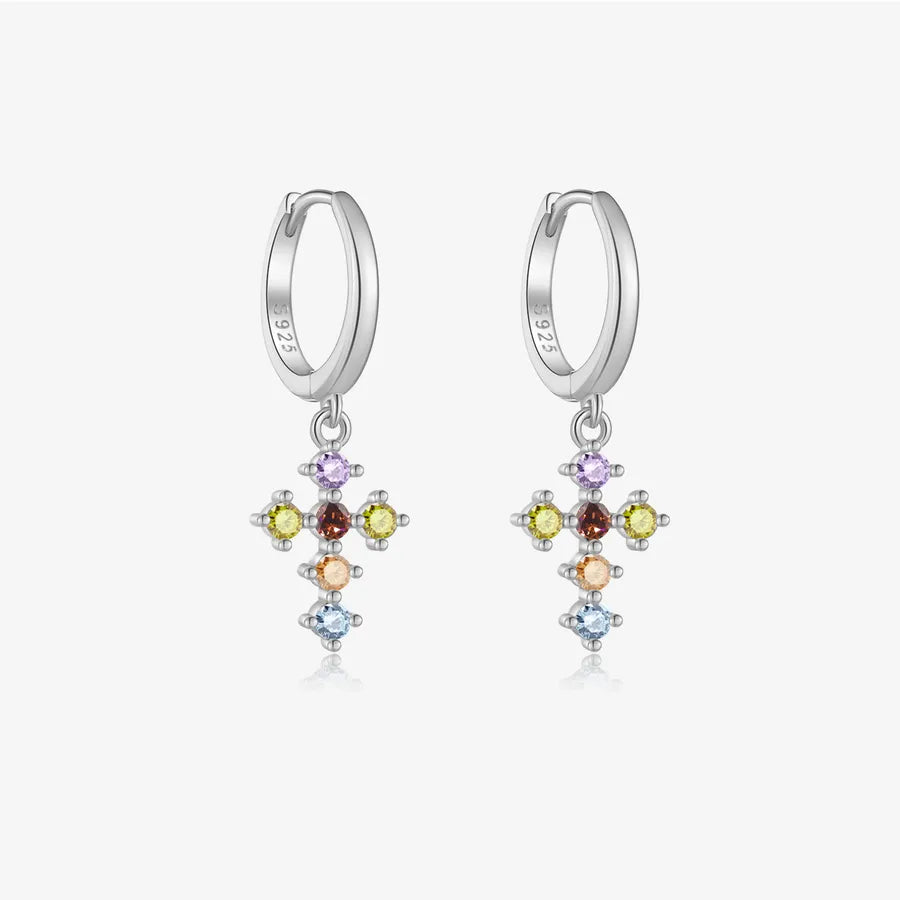 A pair of sterling silver huggie hoop earrings with dangling multi-colored gemstone crosses, shown on a light gray background.