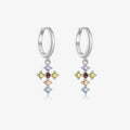 A pair of sterling silver huggie hoop earrings with dangling multi-colored gemstone crosses, shown on a light gray background.